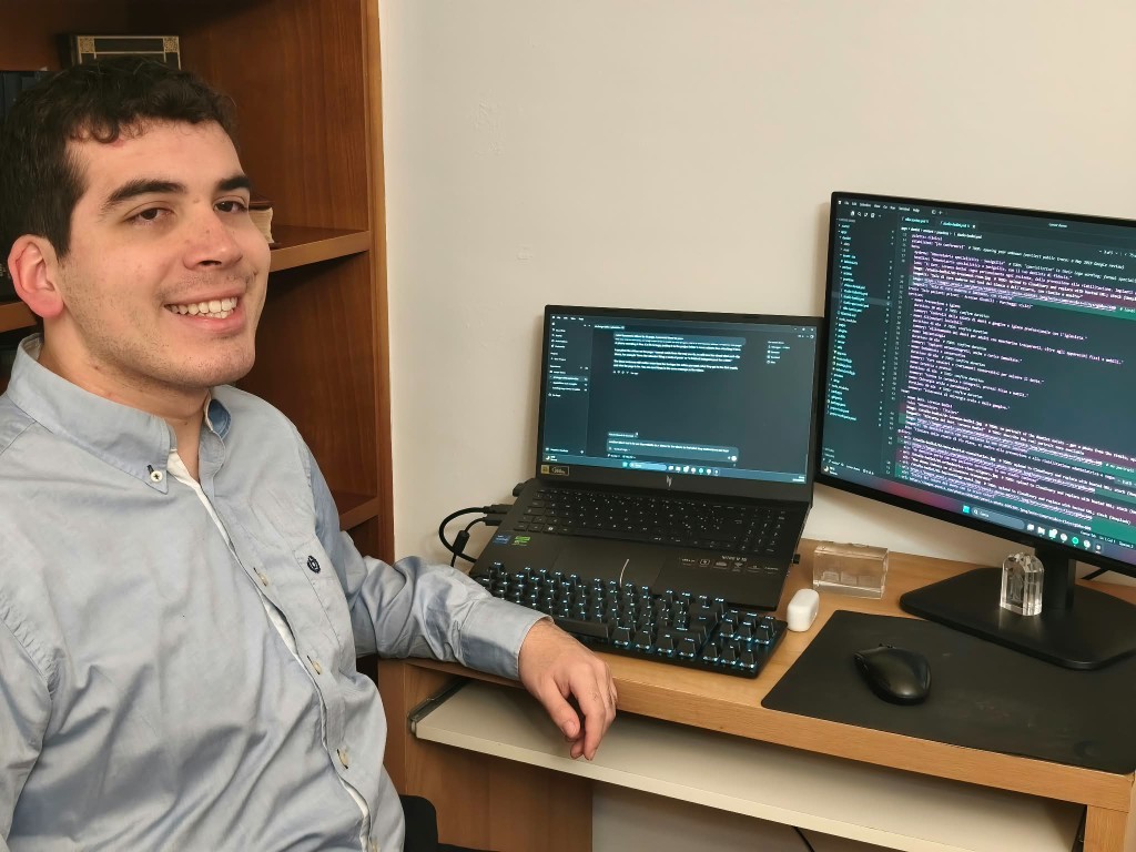 Mauricio sorride alla scrivania, accanto al portatile e al monitor